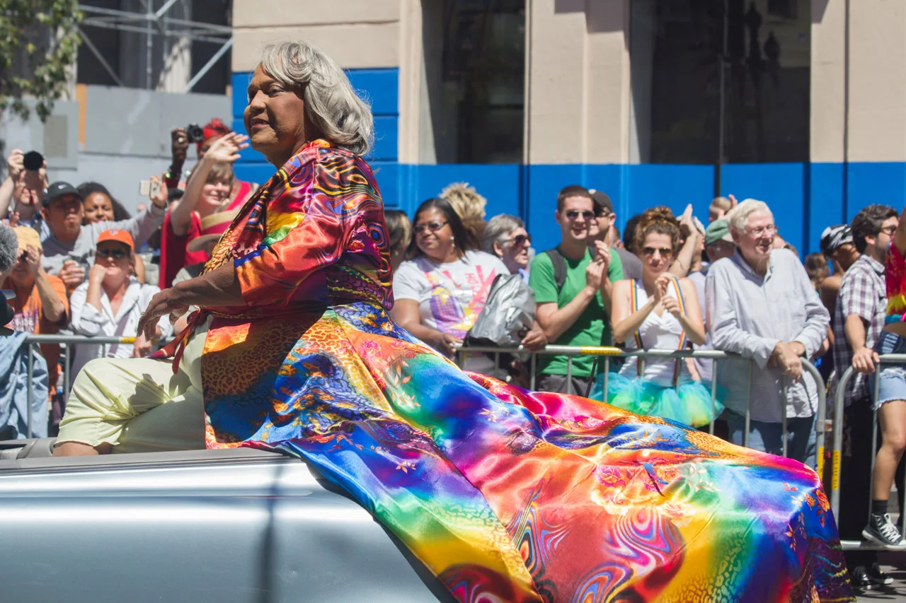 Miss Major wears a rainbow coat and sits in a convertible at Pride.